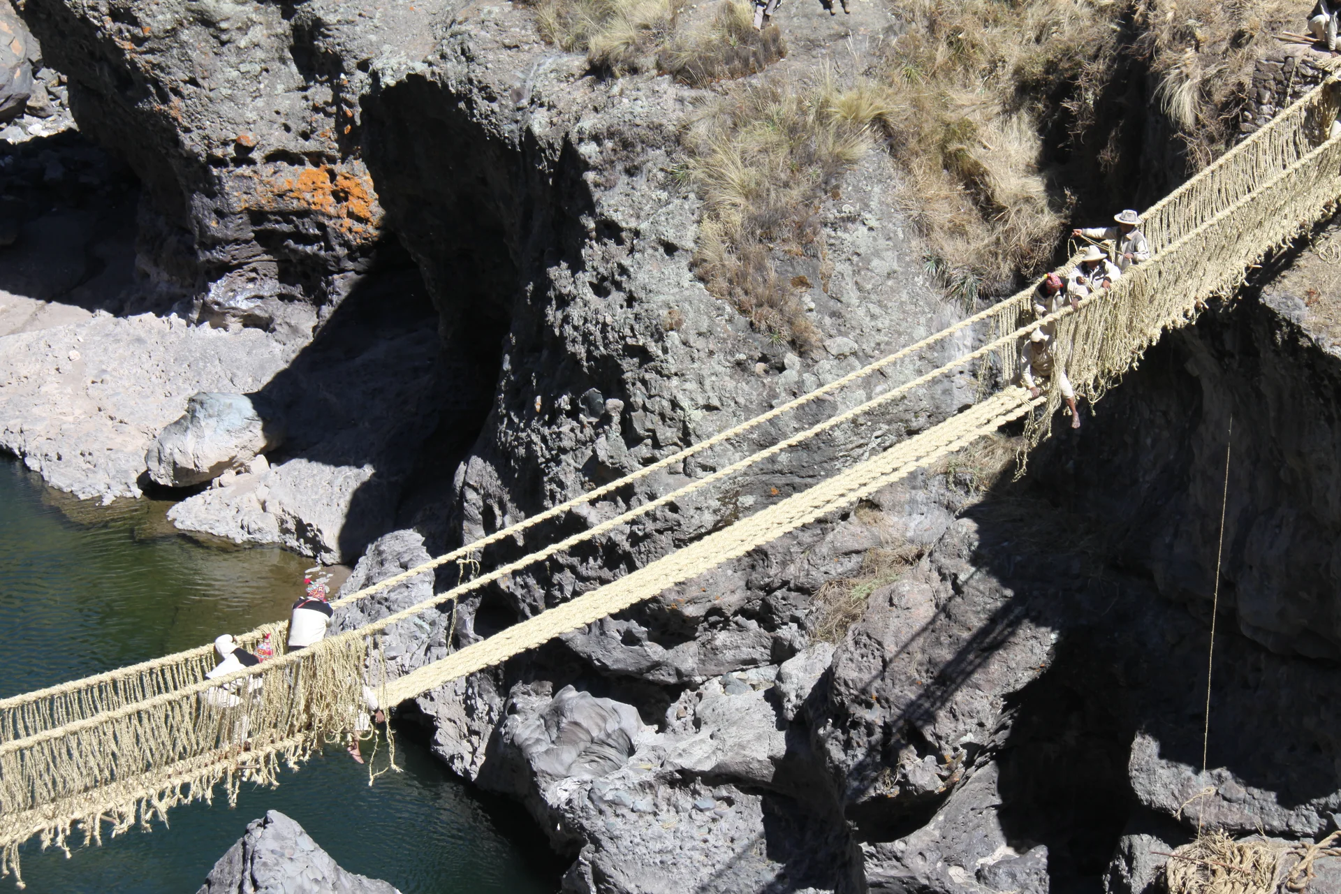 Constructores trabajan en el puente tejido Q’eswachaka sobre el agua entre paredes rocosas escarpadas.